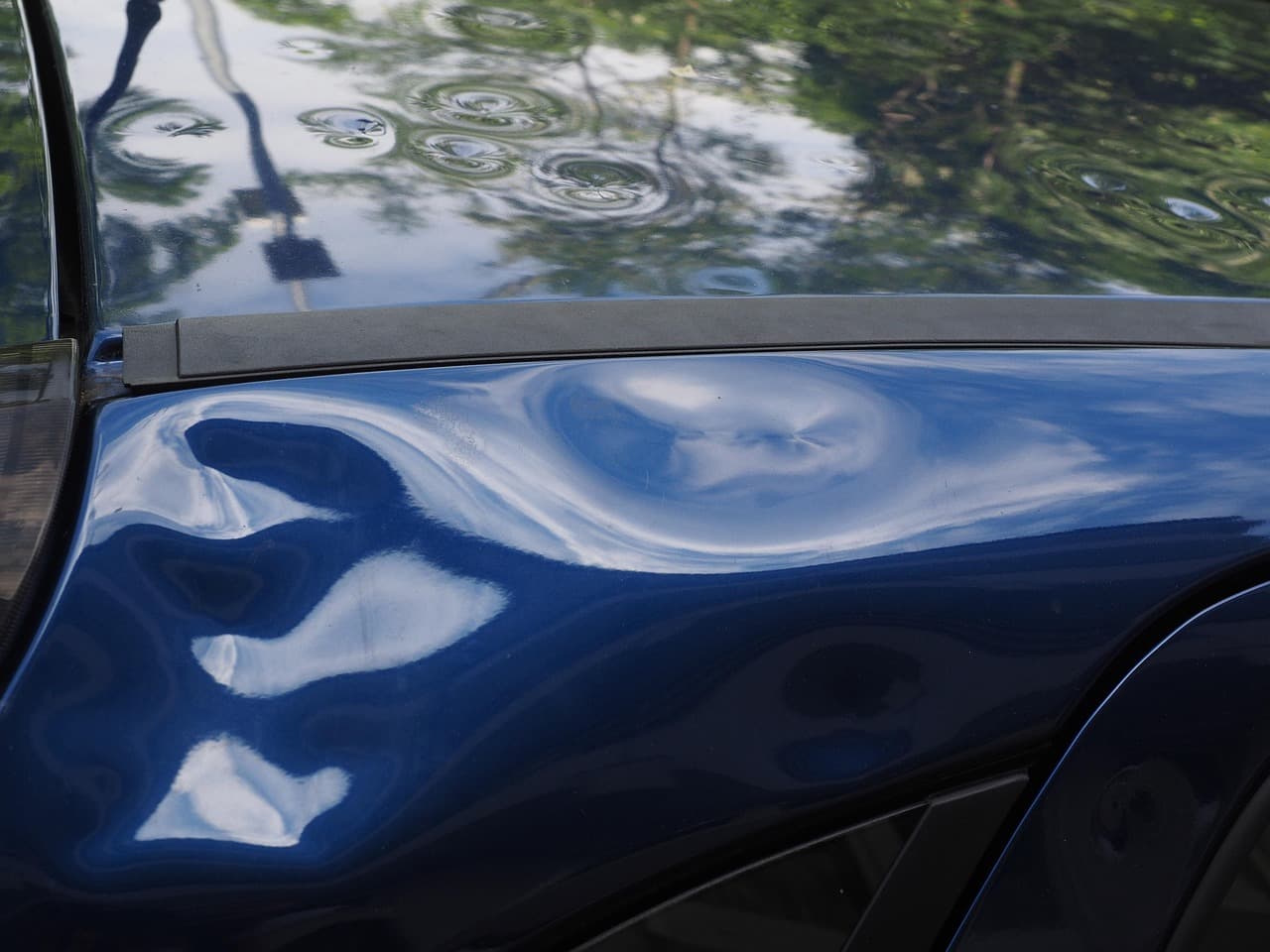 Small dents rippling the reflections on a dark blue car panel
