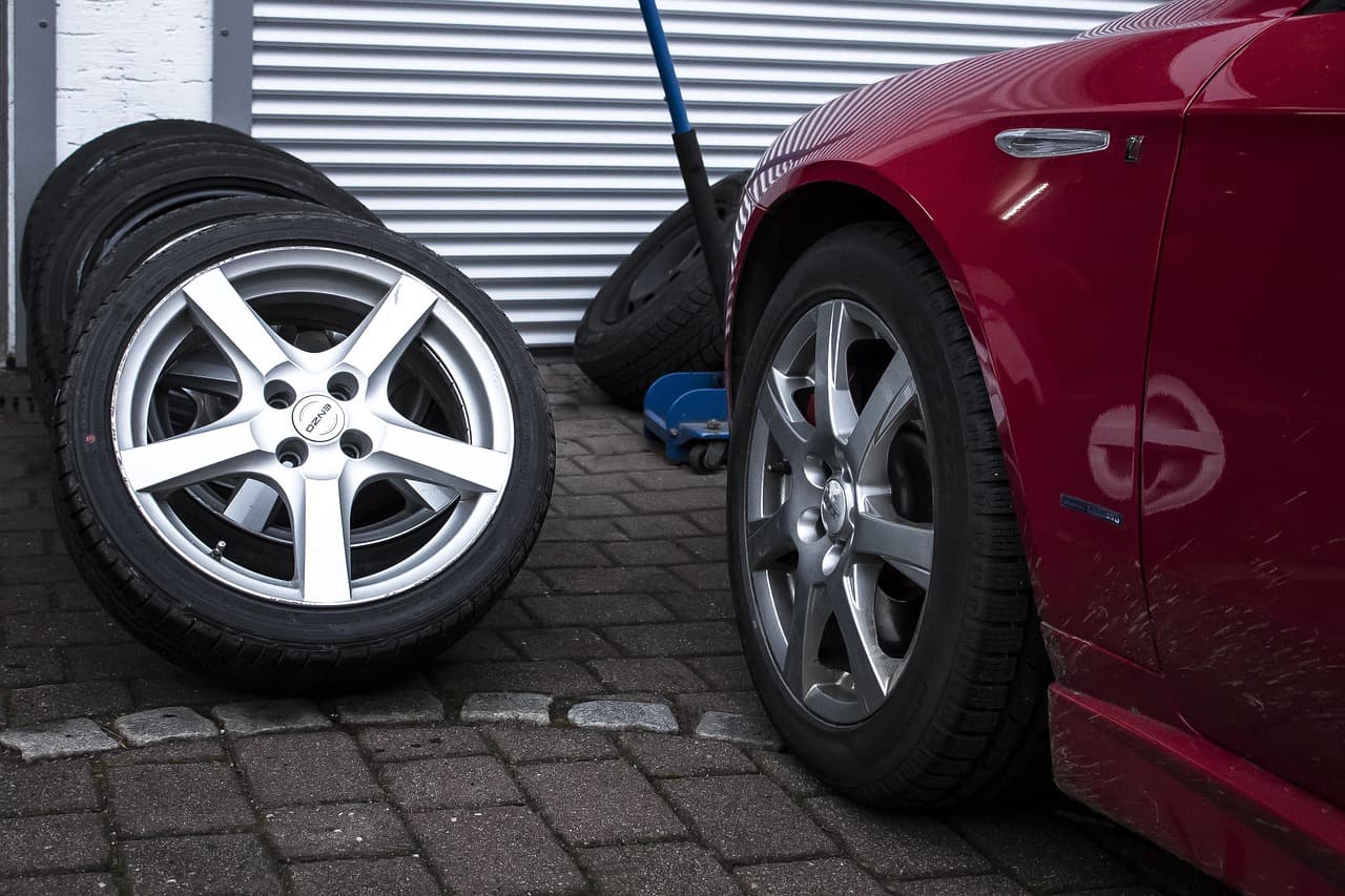 Alloy wheels and tyres stacked by a roller shutter, a red car beside them