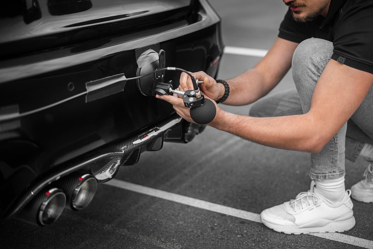A technician crouched at the back of a car, holding a test probe to the tailpipes