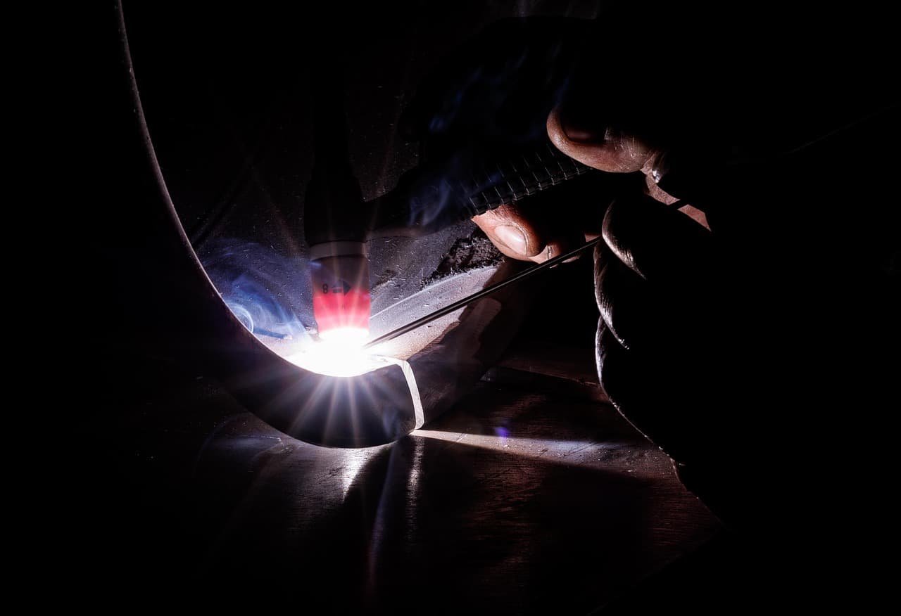 A TIG weld glowing along a curved metal edge in a dark workshop
